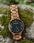 Rootstone SKOGTIND Männeruhr aus Snakewood und Metall mit schwarzem Zifferblatt auf moosigem Stein